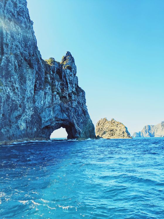 Rock formation with a large arch over blue ocean waters under a clear sky, with smaller rocky islands in the background.
