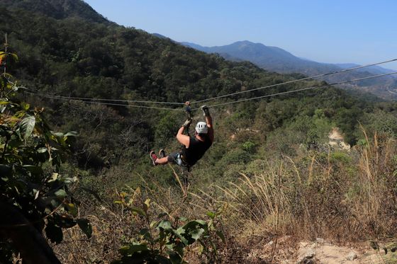 Person ziplining over a lush, mountainous landscape with a clear blue sky in the background.