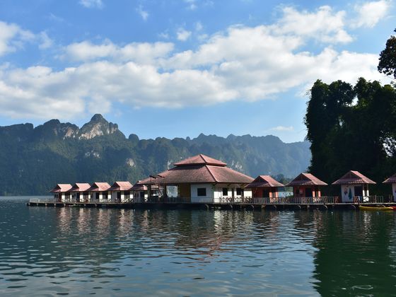 Floating bungalows on a serene lake with mountain backdrop and blue sky with clouds.