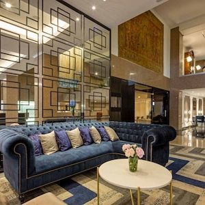 Luxurious hotel lobby with a blue tufted sofa, geometric wall design, elegant lighting, and a round white table with flowers.