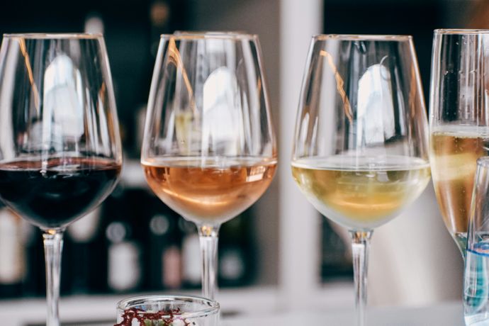 Four wine glasses filled with red, rosé, white wine, and champagne on a table, with a blurred background of bottles.