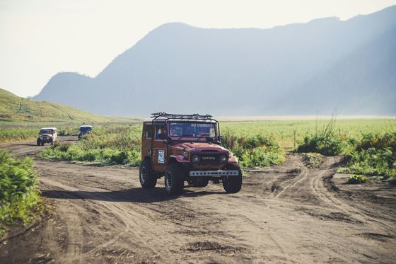 Off-road vehicles driving on a dirt path through a grassy landscape with mountains in the background under a clear sky.
