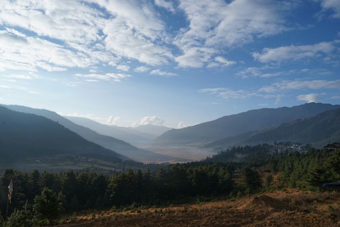 Scenic view of a valley with mountains under a partly cloudy sky, lush greenery, and a small village in the distance.
