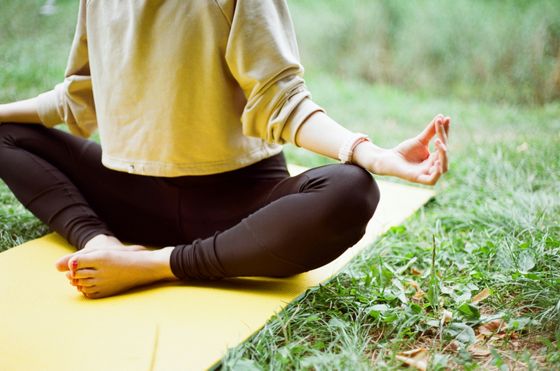 Person meditating in a cross-legged position on a yellow yoga mat outdoors, surrounded by grass.