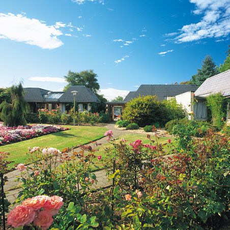 A garden with vibrant roses and manicured lawns surrounded by quaint cottages under a clear blue sky.