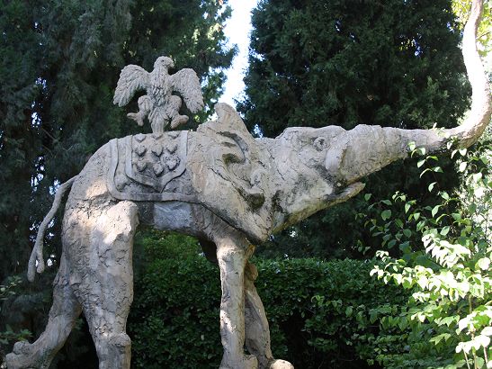 Stone elephant statue with an eagle on its back amid lush greenery and trees.