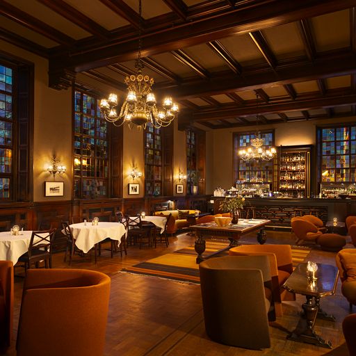 Elegant restaurant with high ceilings, stained glass windows, white tablecloths, and a central lounge area with a bar in the back.