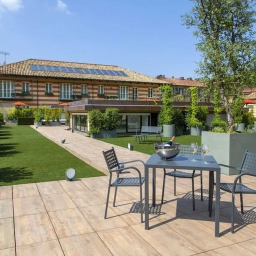 Rooftop patio with a table, chairs, and a wine bucket. Surrounded by greenery, with a view of a large building under a clear blue sky.