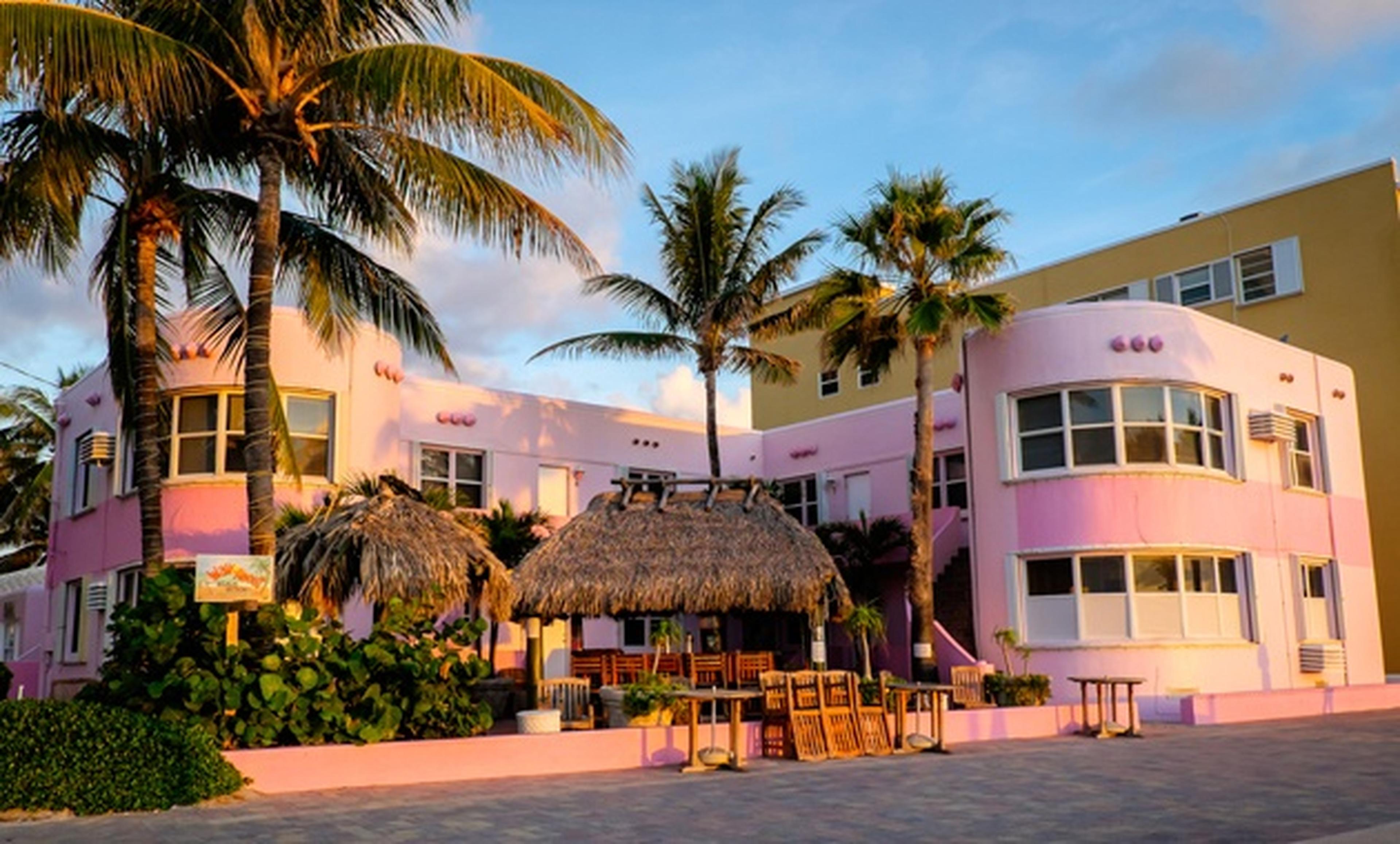 palm trees in front of pink building with tiki hut