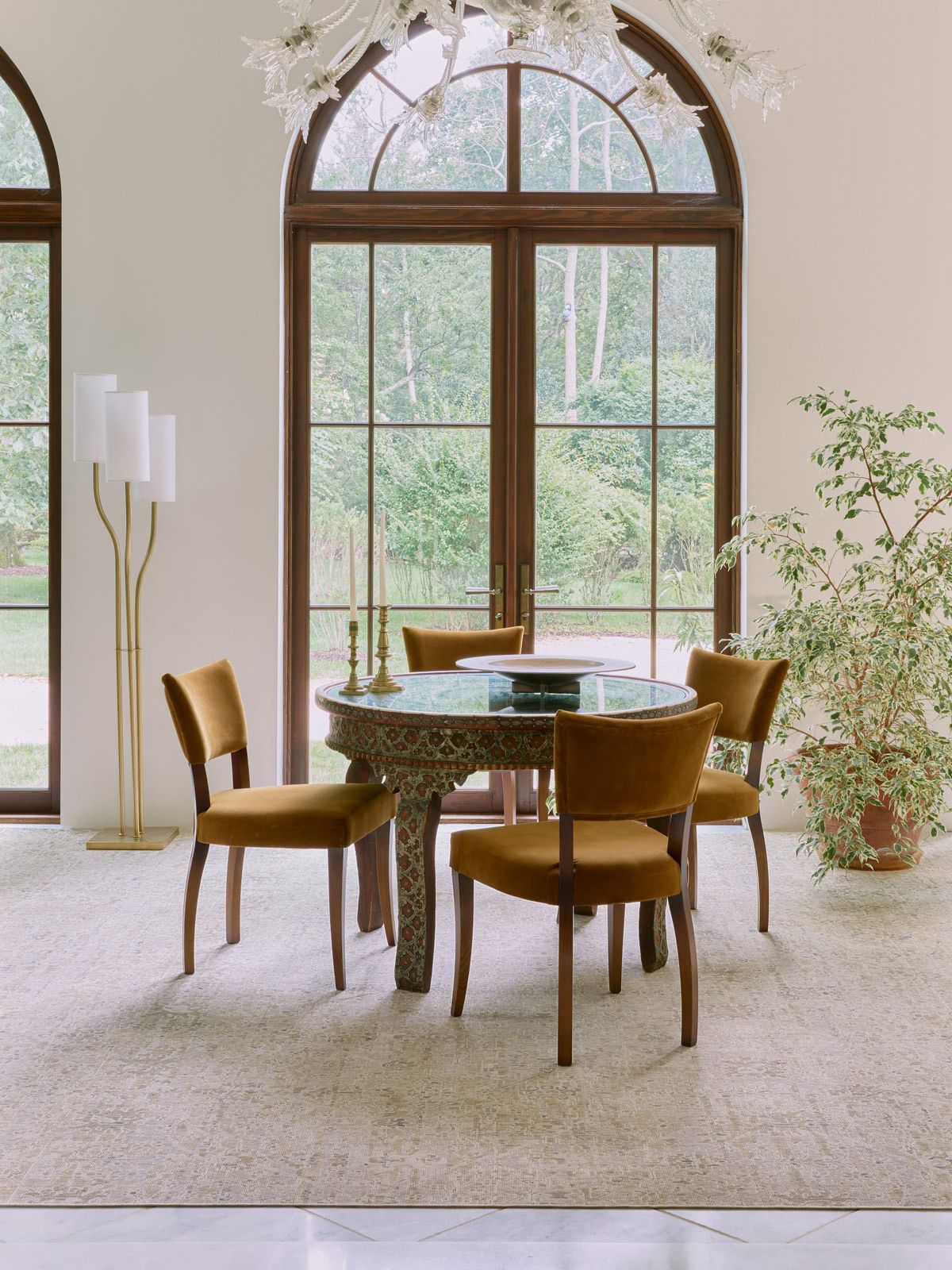 A patterned Persian rug in beige and tans lays under a small dining room table in the center of the room with a large window behind it