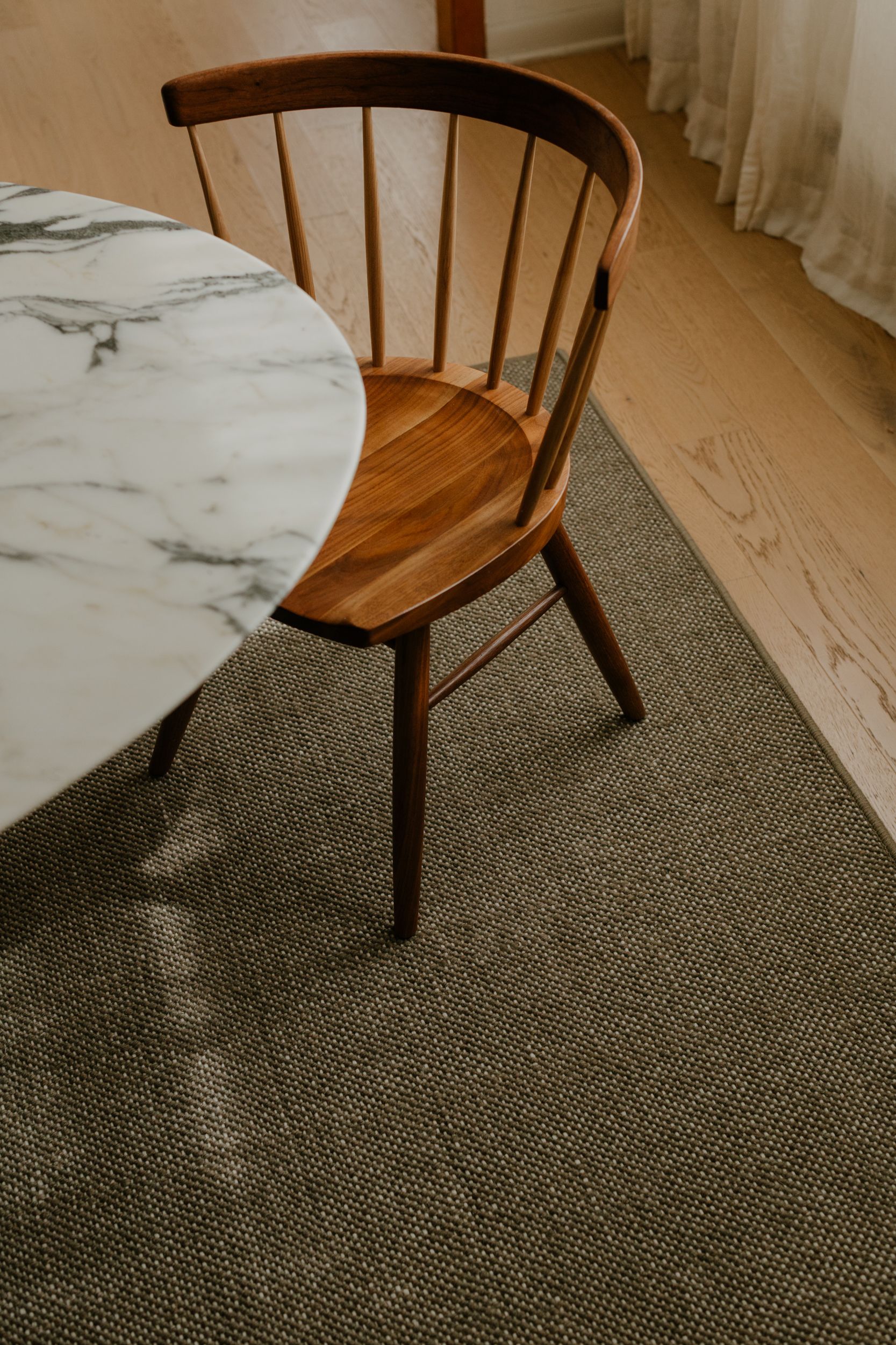 dark green rug under dining room table and single  chair over hardwood floors 
