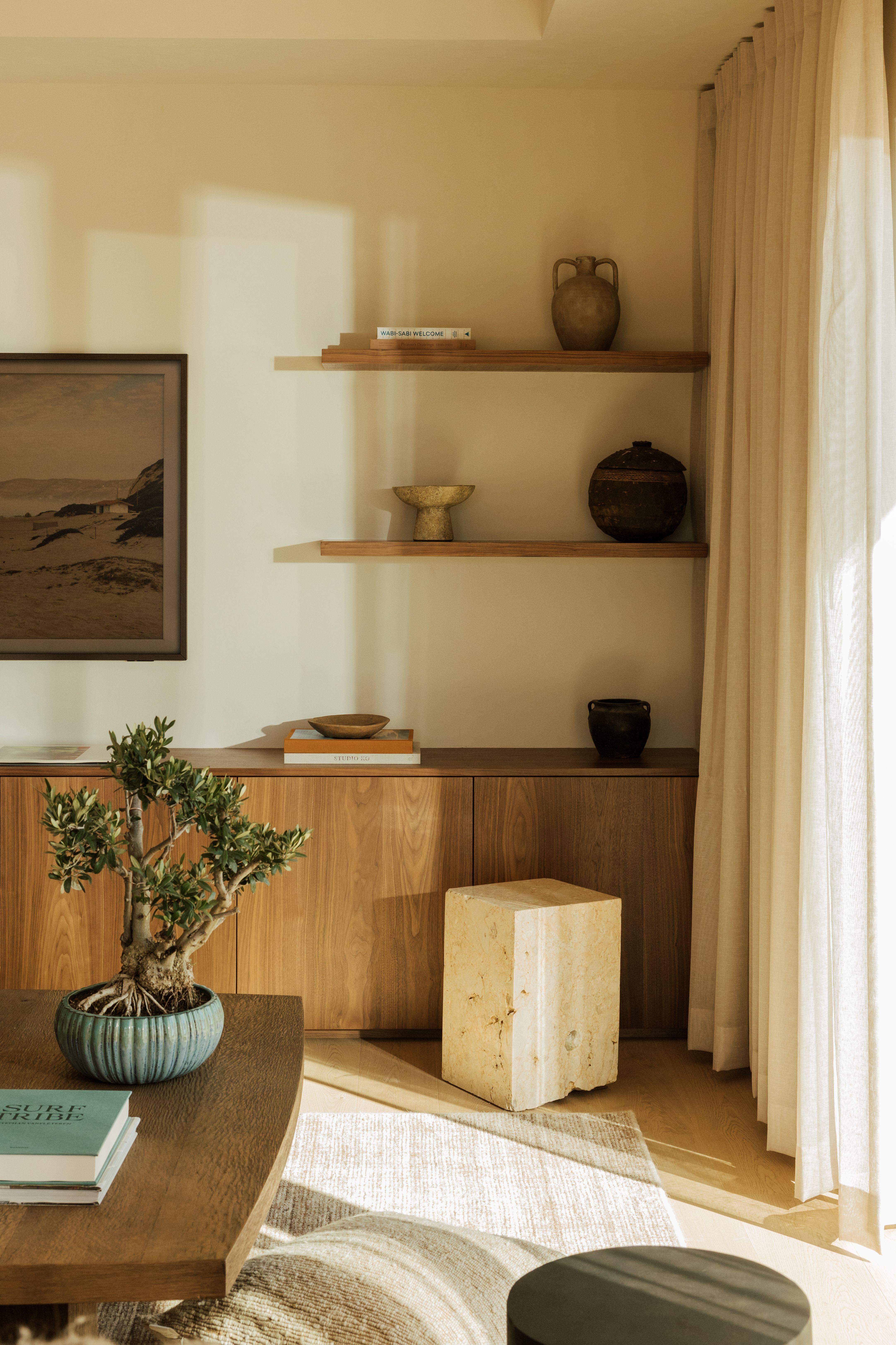 Media room corner with floating wood shelves of pottery, a walnut cabinet, a stone side table and a bonsai on the coffee table, over Xander in Cedar