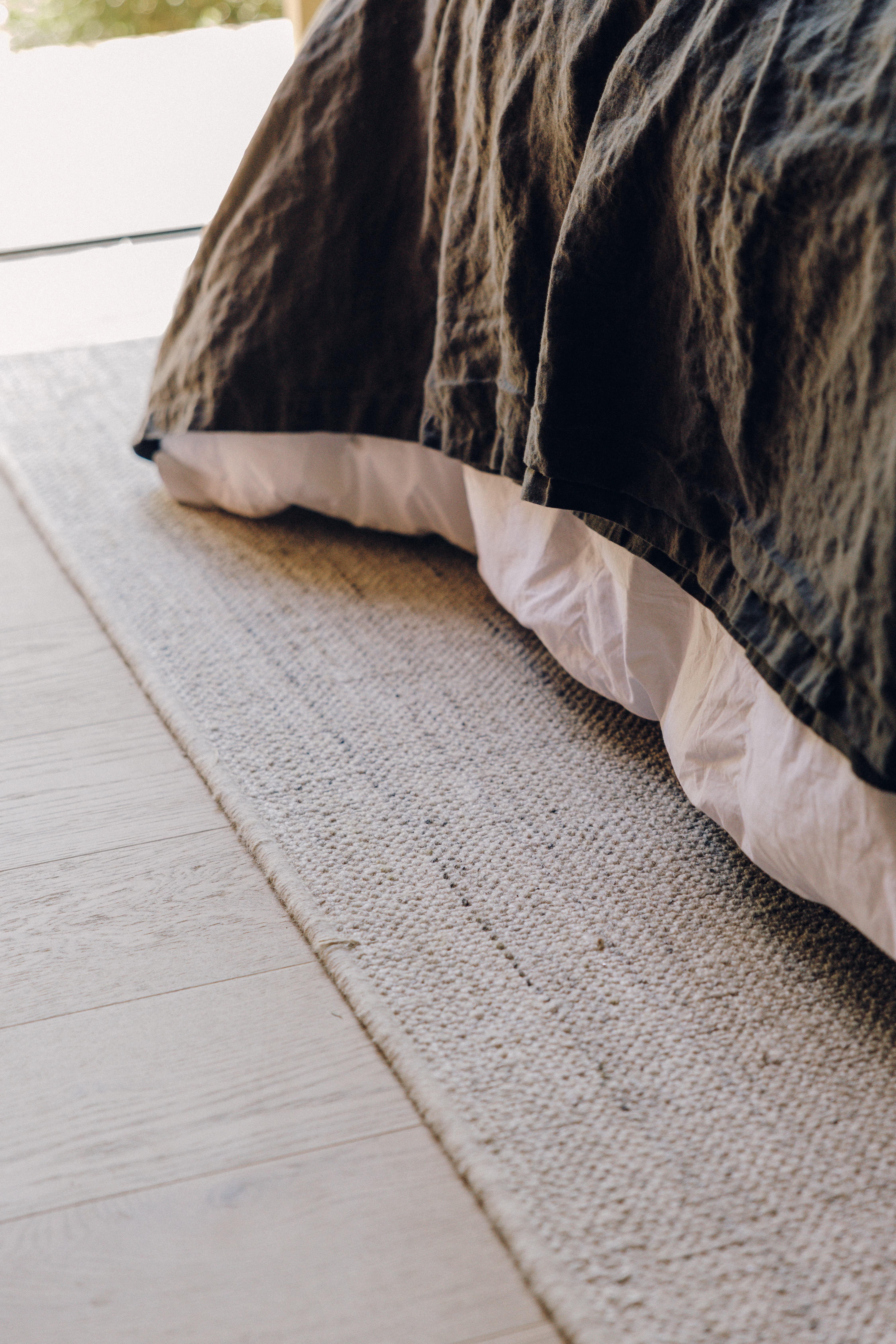 Close-up of a dark linen duvet over white bedding, resting on Maycomb in Linen on pale wood floors