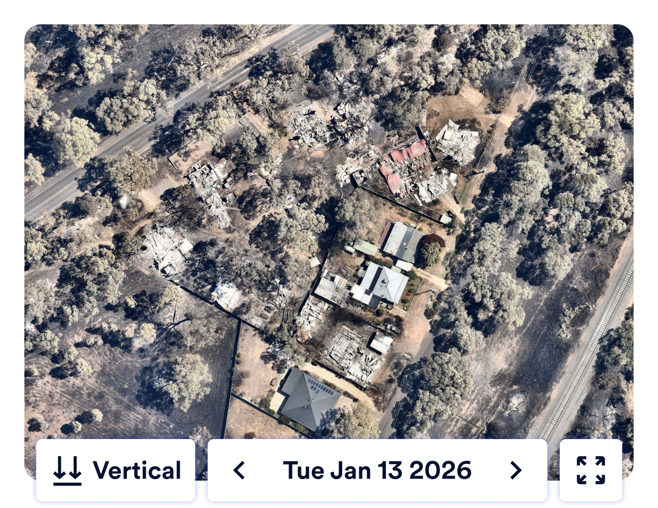 Aerial view of a rural area from Tuesday 13th Jan 2026 showing bushfire damaged and burnt structures surrounded by trees. Roads are visible on the left and right sides.