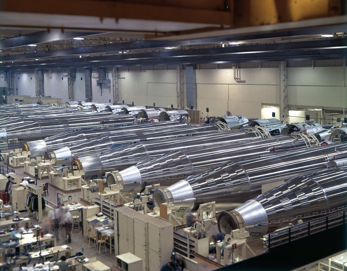 Dozens of Atlas SM-65 missiles lying on their side in a production line at a factory in San Diego, from 1961. The rockets are a shiny metallic colour and being assembled.