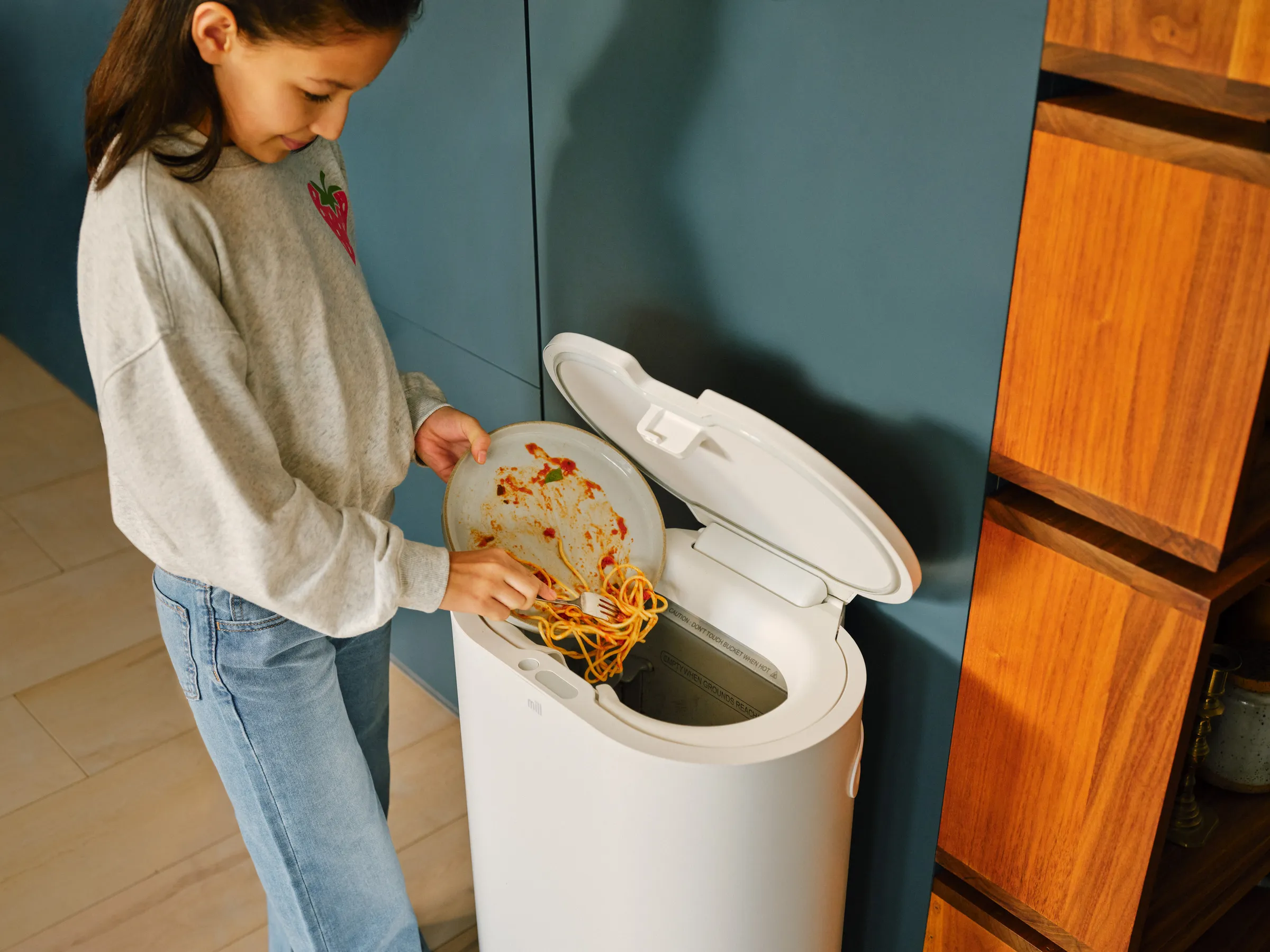 Lunch leftovers being added to a Mill food recycler in a bright kitchen