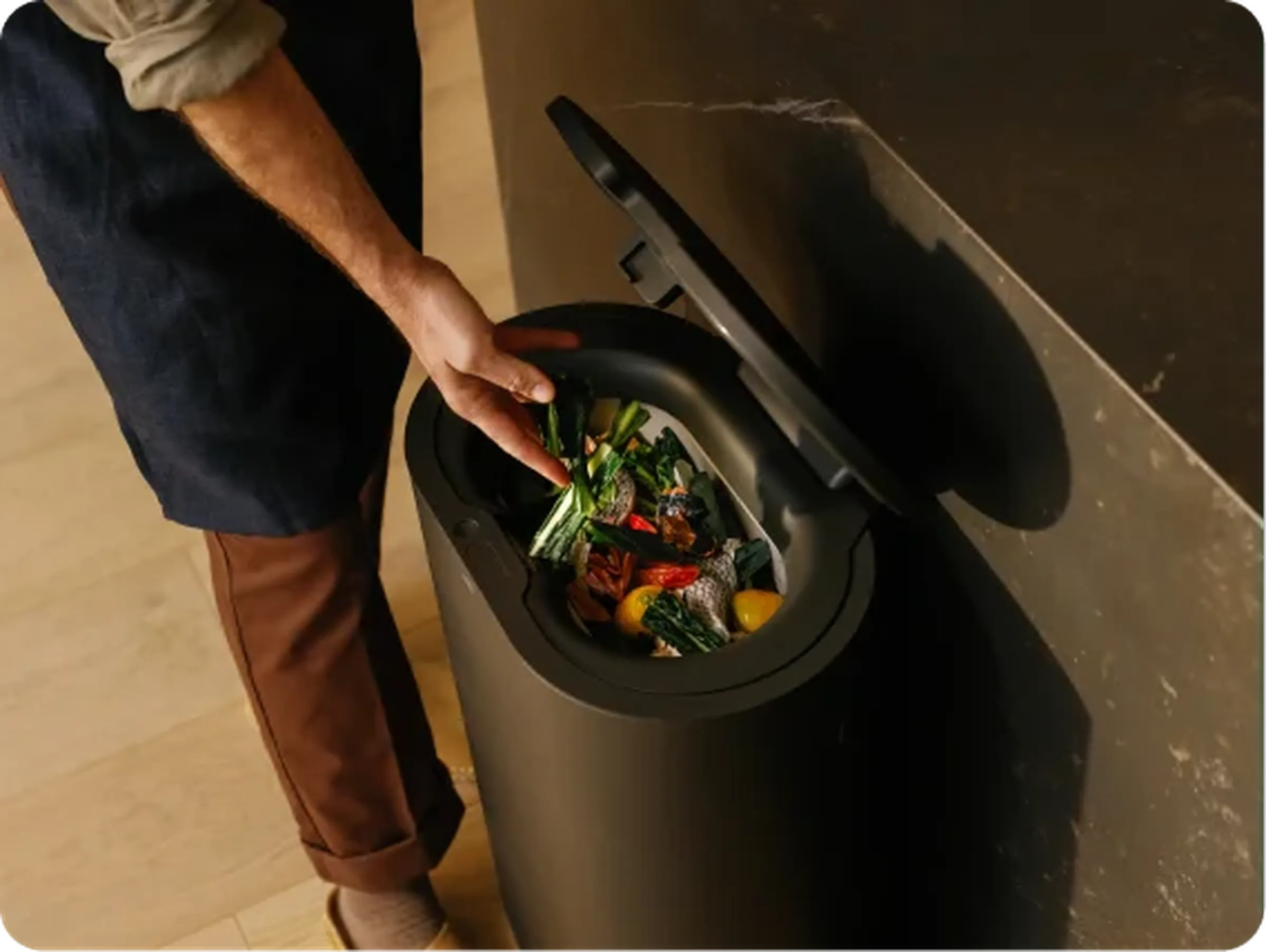 A person dropping vegetable scraps into an open Mill bin