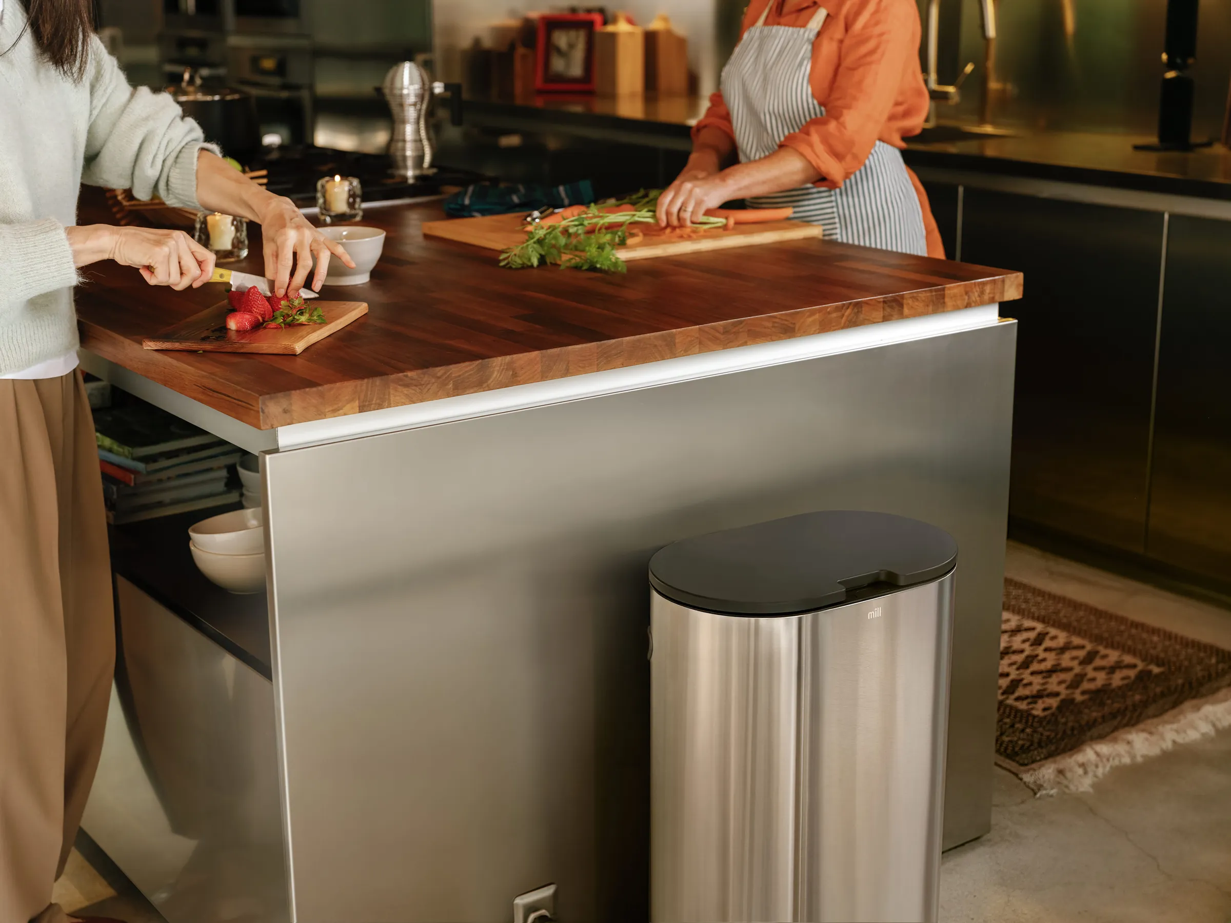 Two people preparing food at a kitchen island beside a Mill bin