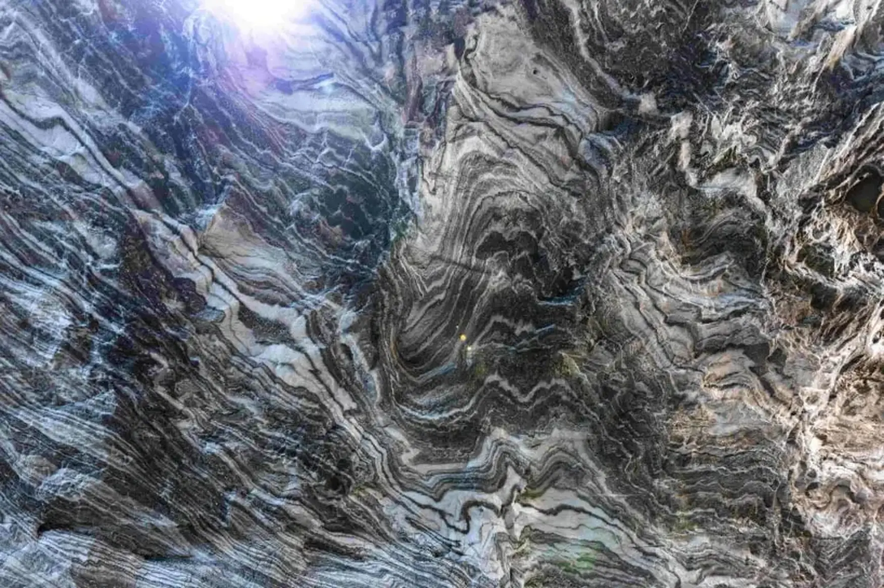 Abstract aerial view of a rugged, swirling landscape with gray and white patterns, resembling marble or rock formations, under bright sunlight.