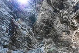 Abstract aerial view of a rugged, swirling landscape with gray and white patterns, resembling marble or rock formations, under bright sunlight.