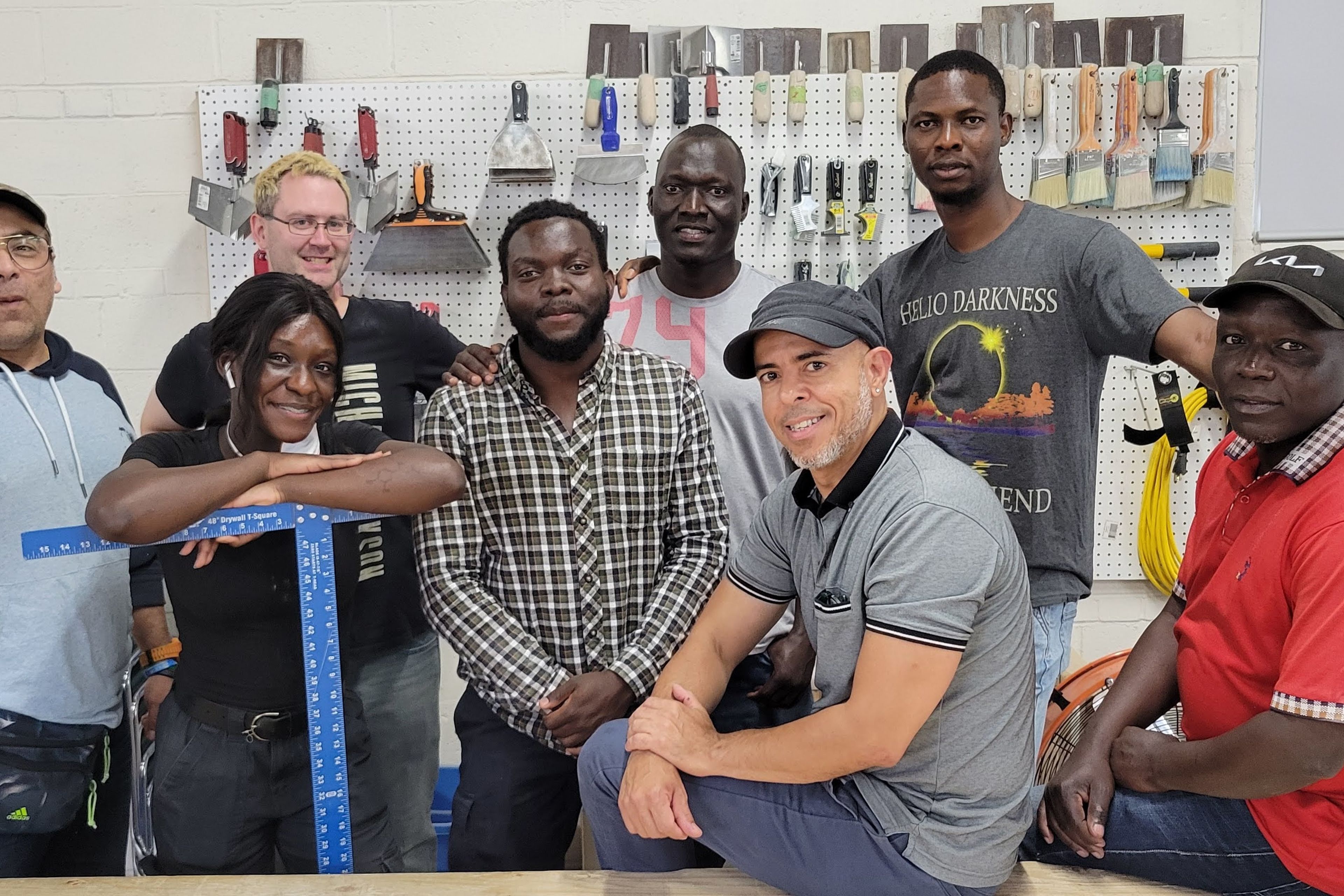 A group of people are standing and posing for the camera. They are surrounded by tools and paintbrushes.