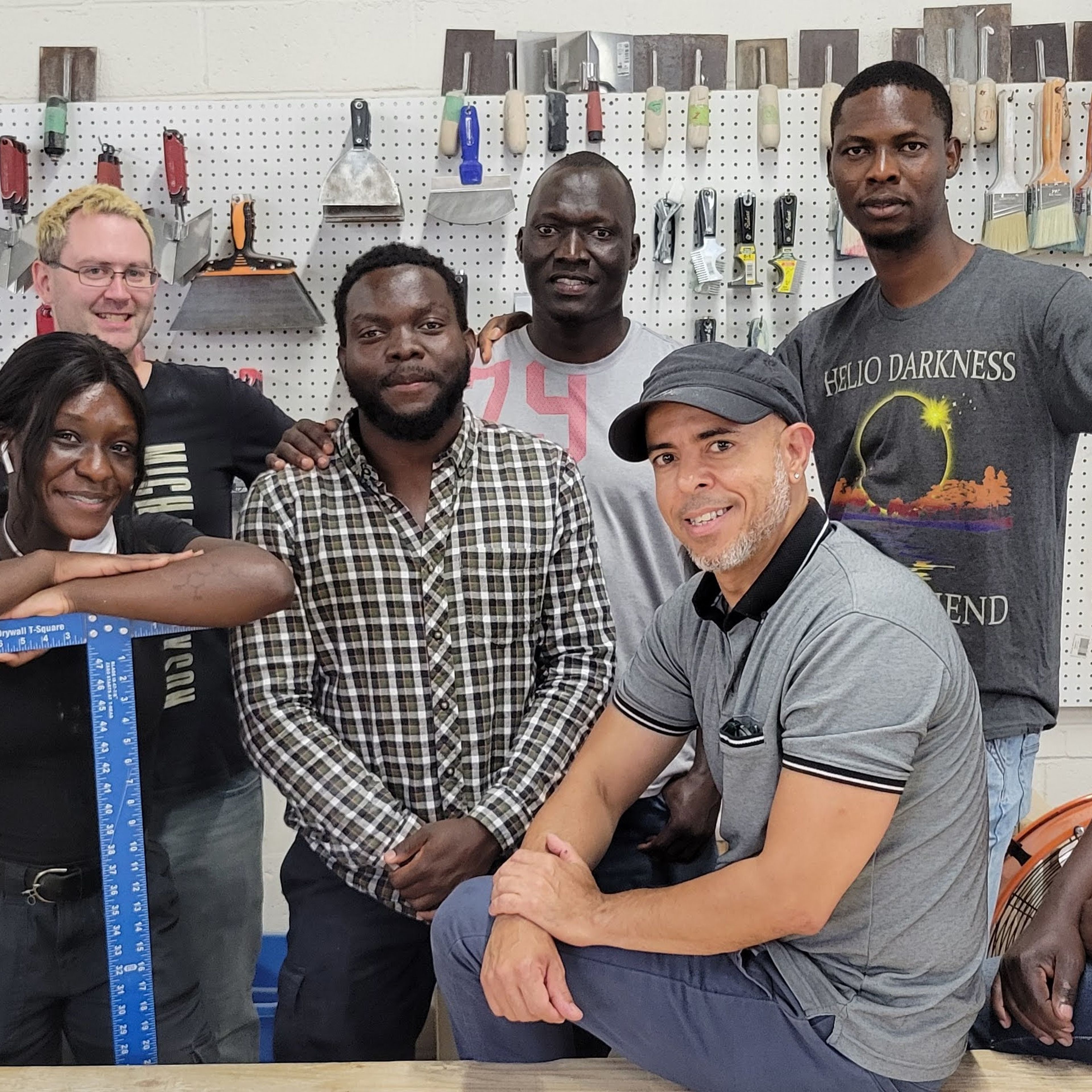 A group of people are standing and posing for the camera. They are surrounded by tools and paintbrushes.
