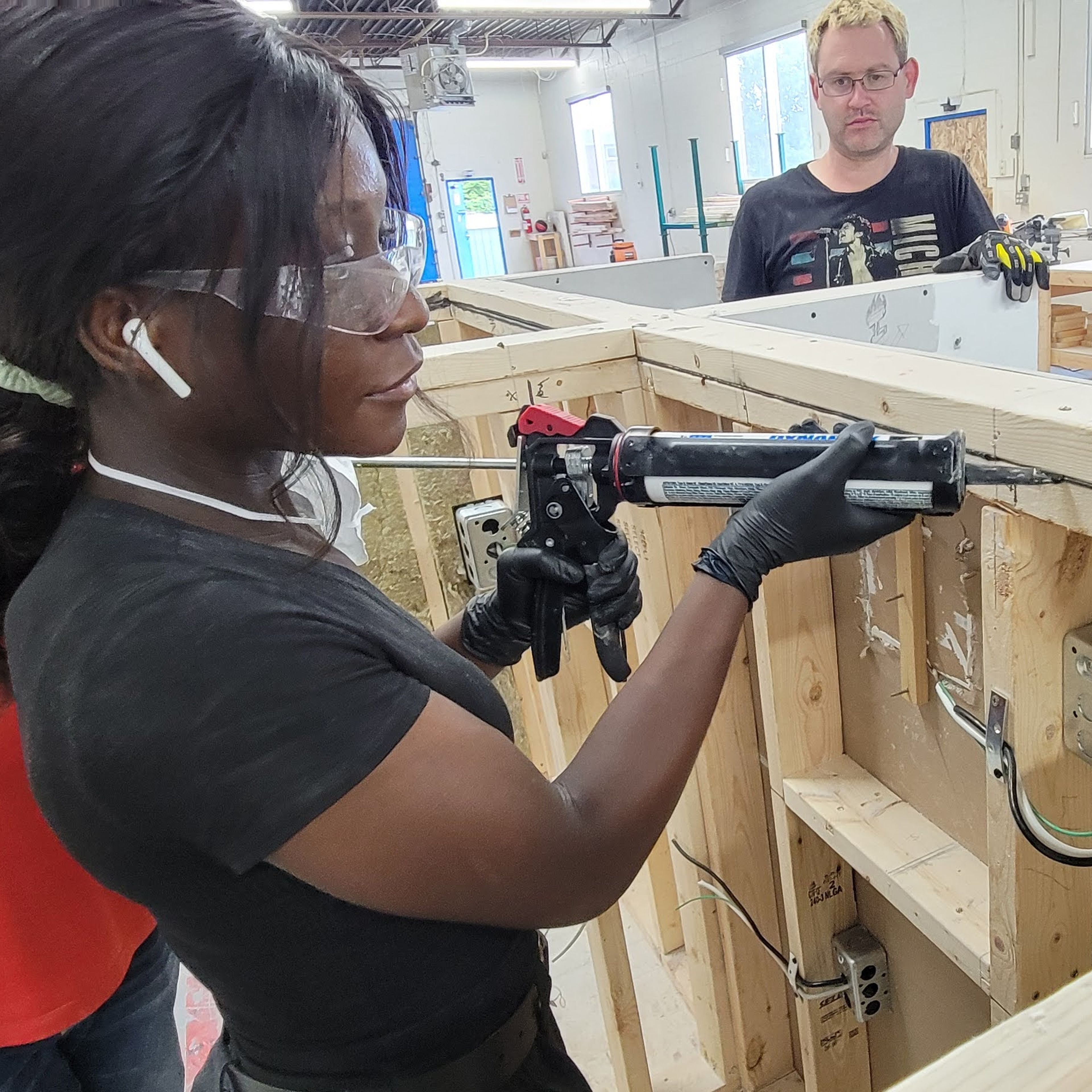 A woman is holding a calking tool and filling in a cap between two pieces of wood.