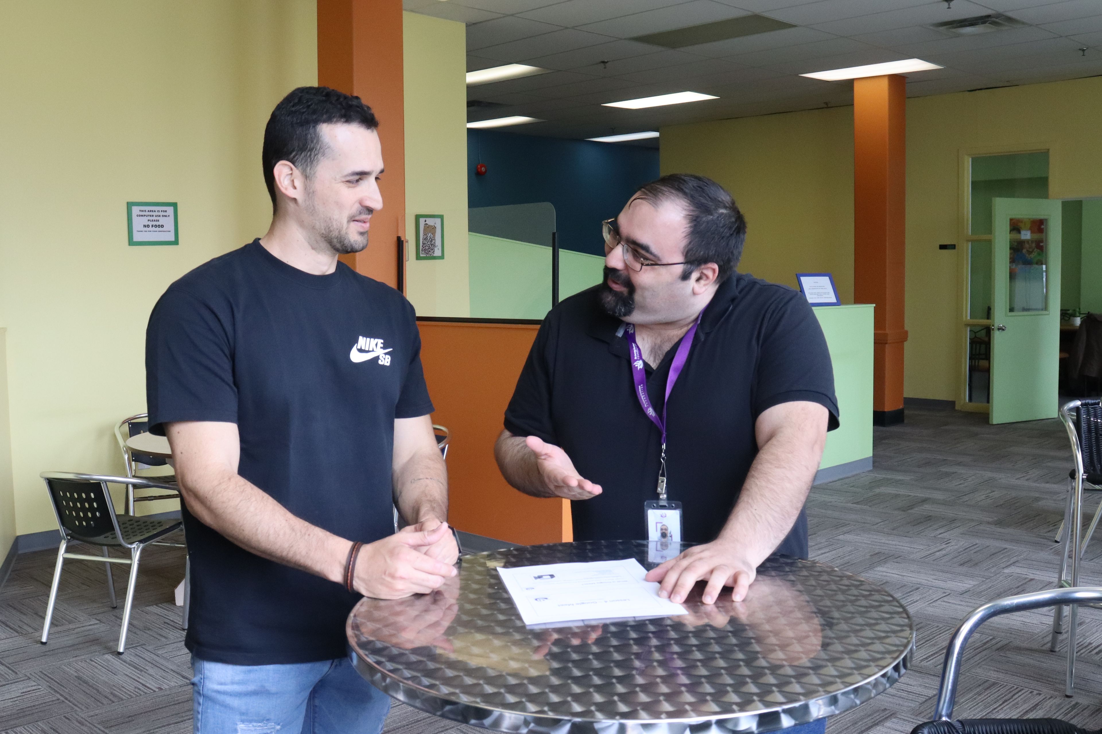Two people standing up and talking at a table.