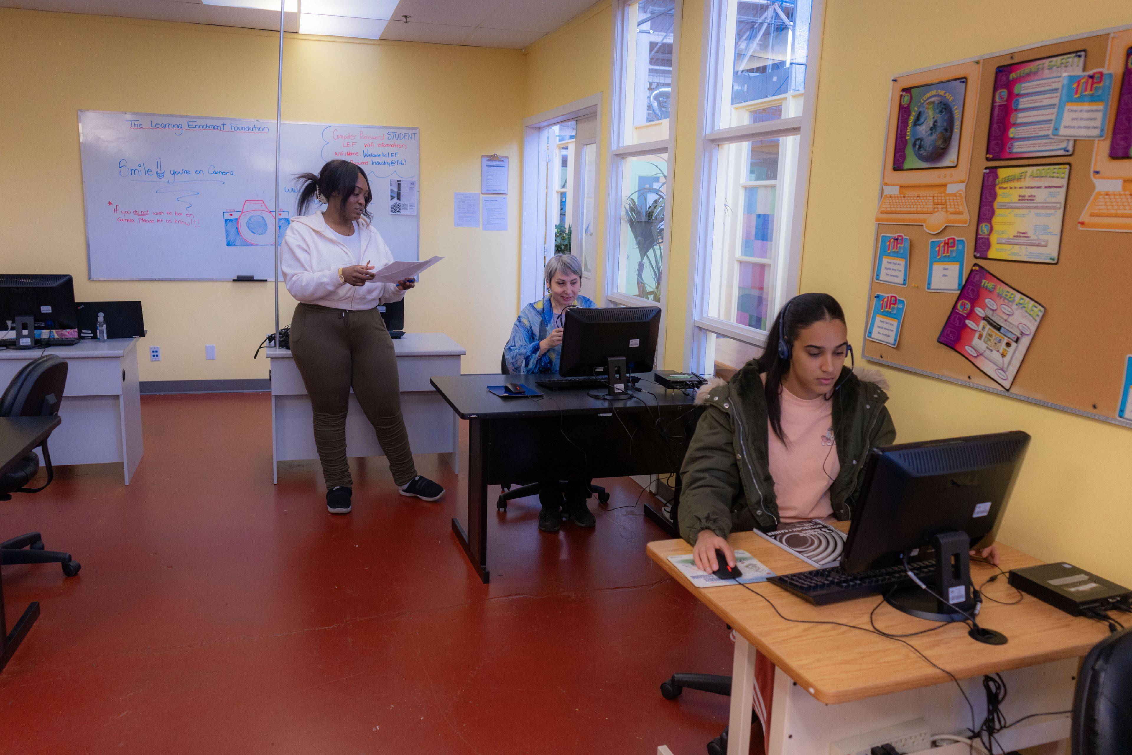 Two people sitting down at a computer and one person standing up.