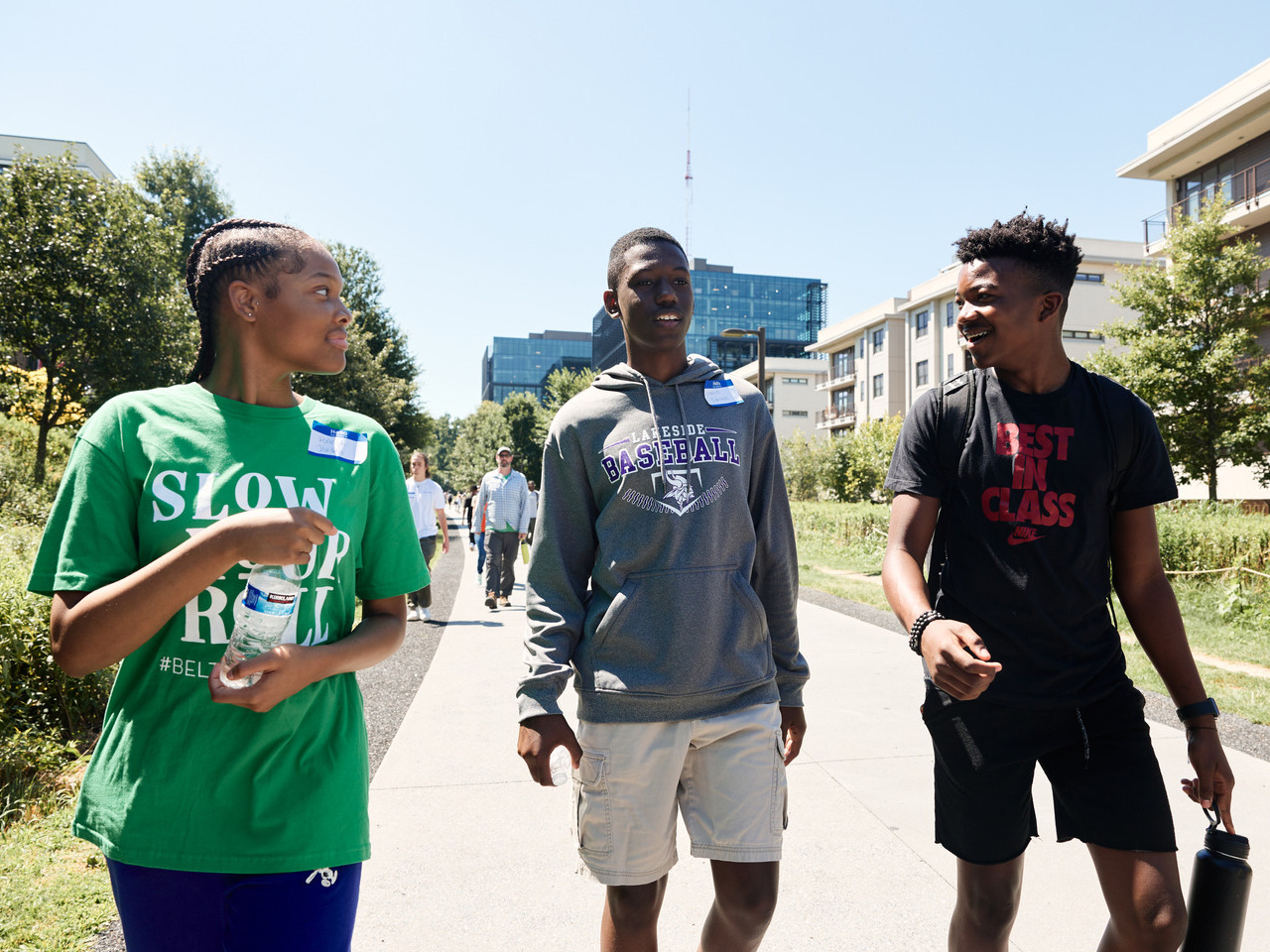 Three teenagers walk together along the Beltline, smiling. Around them are large buildings and greenery.