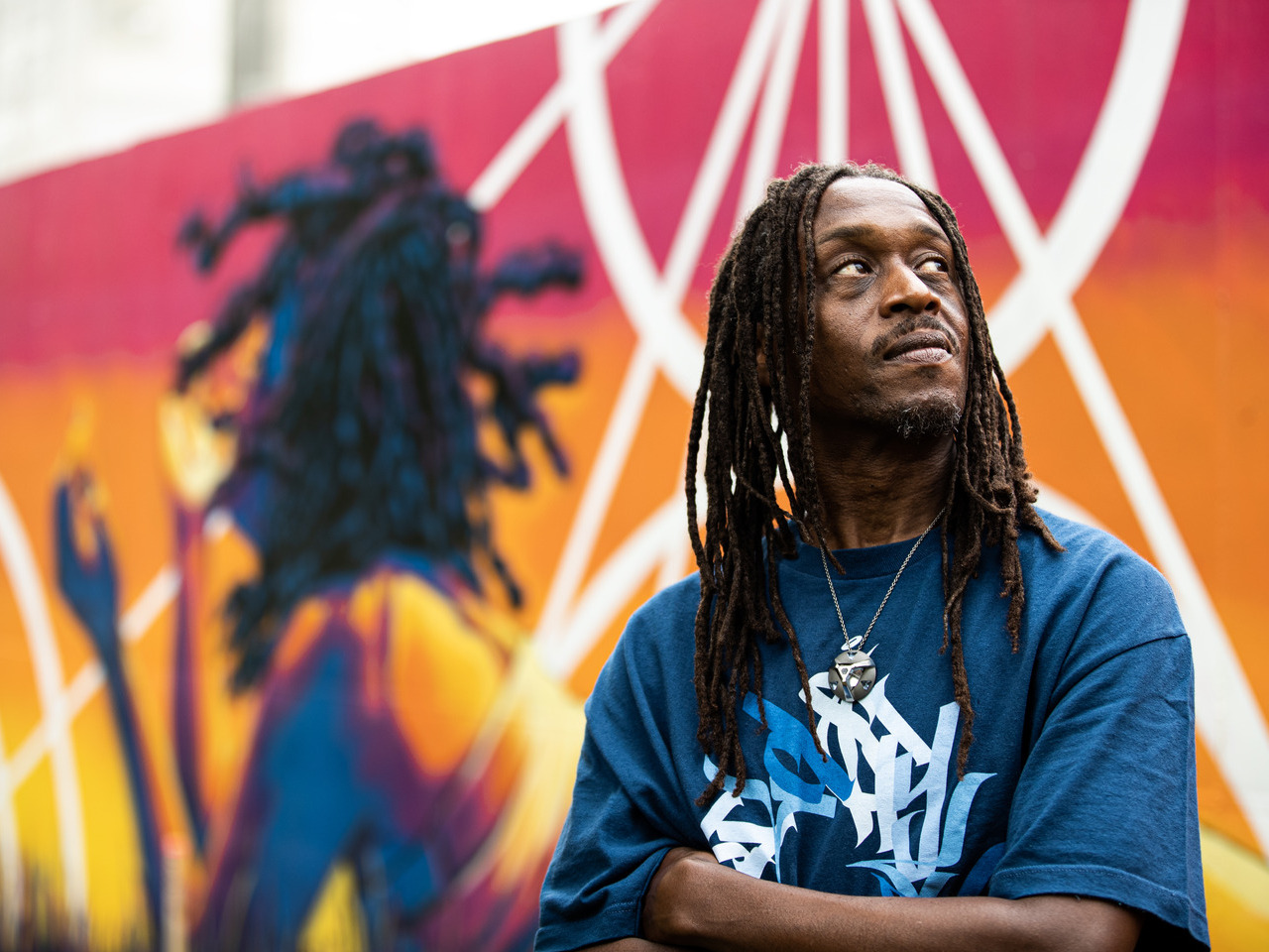 A man stands in front of a colorful mural he painted.