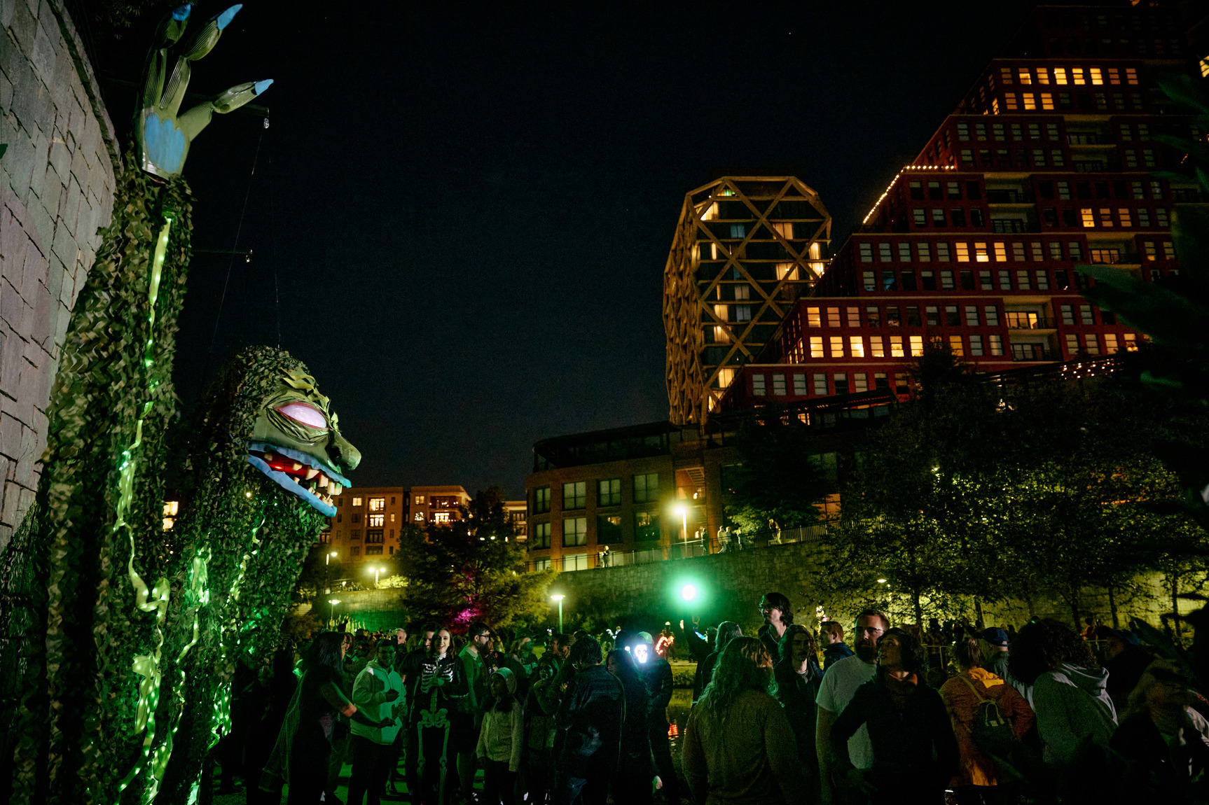 Night event with a large green puppet, illuminated buildings, and a crowd of people enjoying the lively atmosphere.