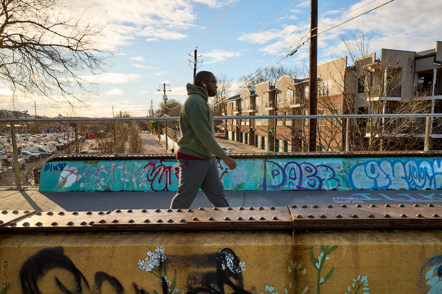 A person wearing a hoodie and sweatpants walks along the Atlanta Beltline with headphones in his ears.
