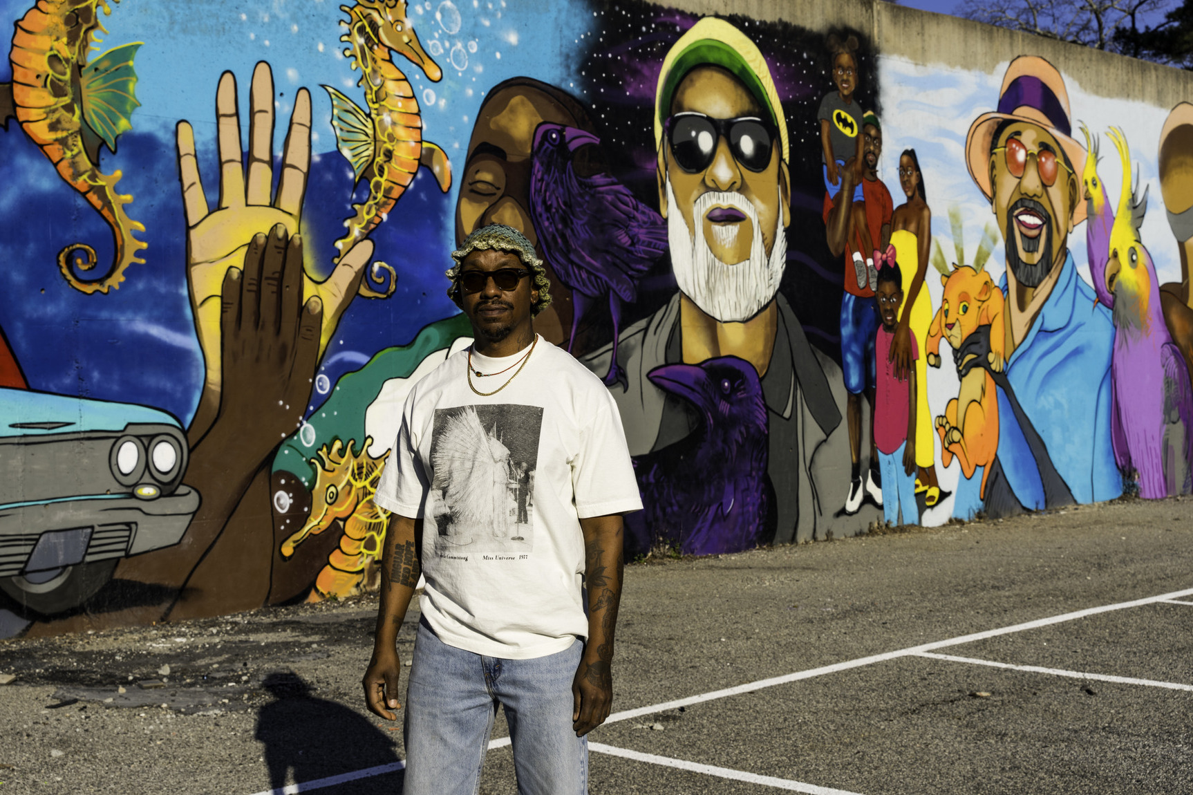 A man stands in front of a colorful mural that depicts several different fathers.