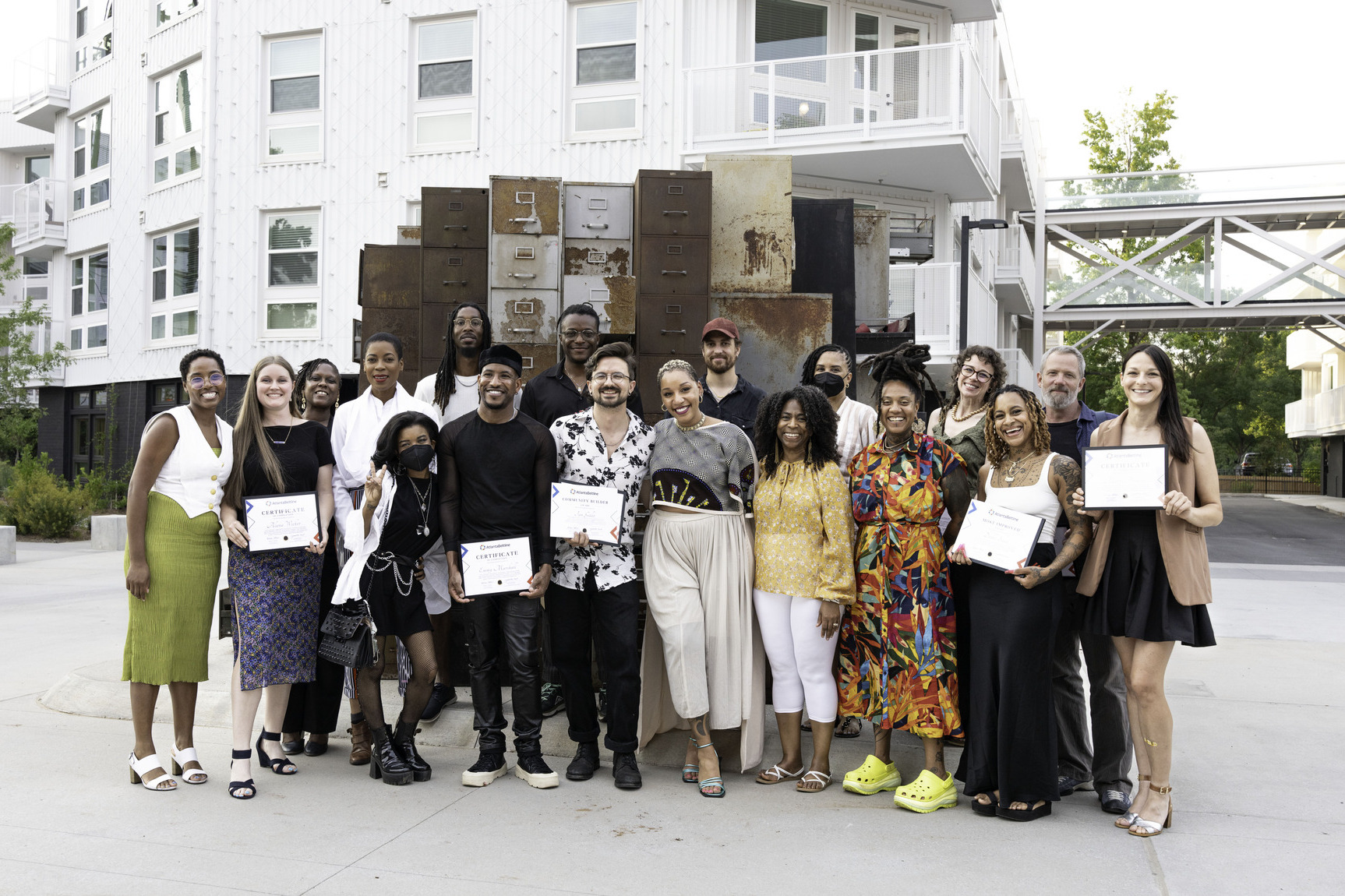 A group of artists pose together outside, smiling and holding graduation certificates.
