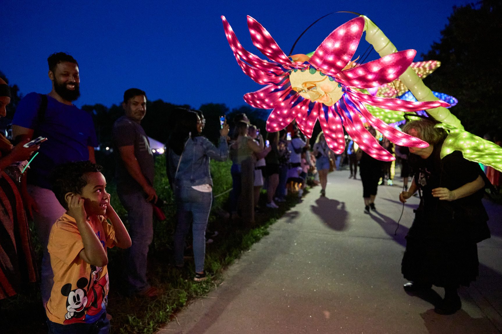 A picture of a child smiling at a large colorful lantern parade shaped like a flower.