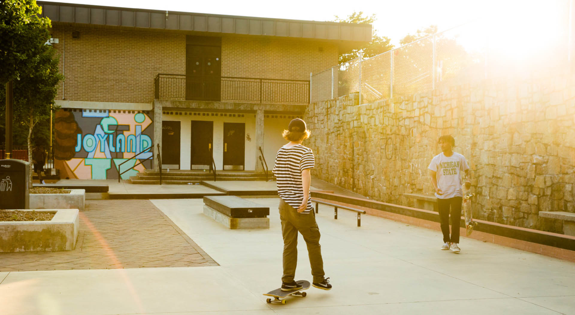 Two young men skateboard in a designated space behind a rec center.