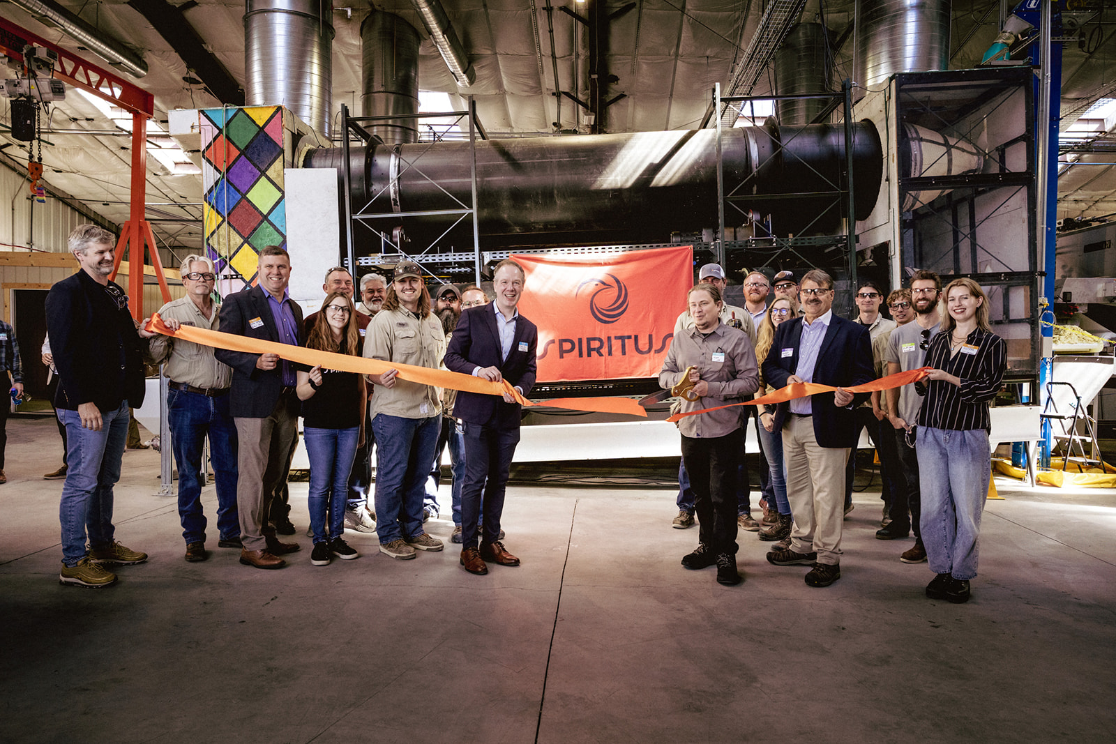 Group of people cutting an orange ribbon at a ceremony, with a "Spiritus" banner in the background.