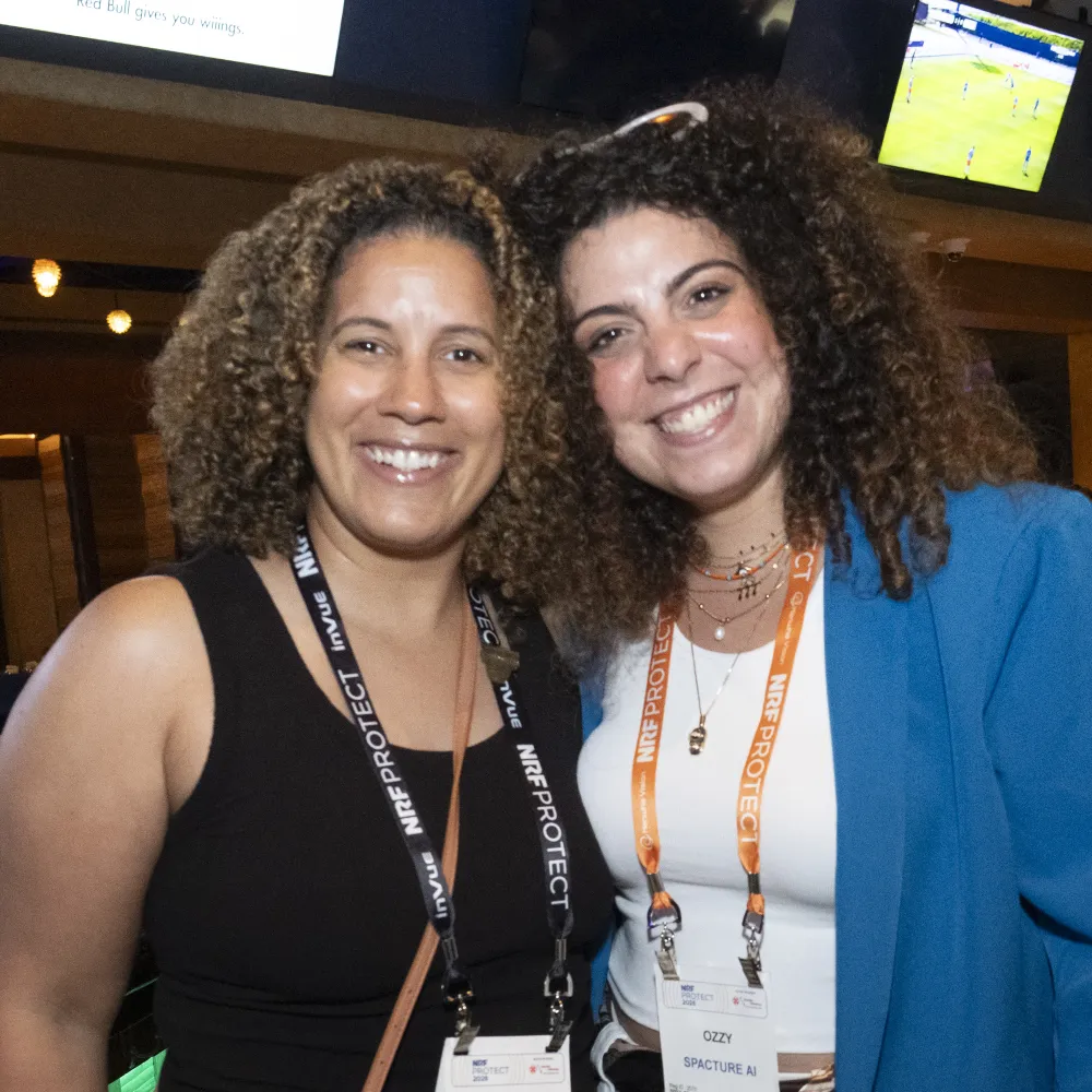 Two conference attendees wearing NRF Protect lanyards pose together at a networking event.