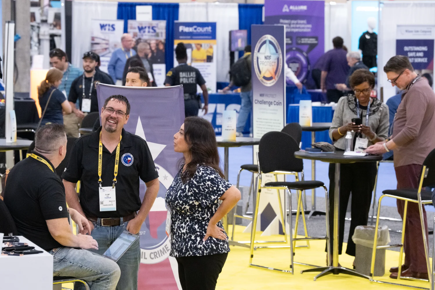 People interacting around the NRF Protect Fusion Center booths with informational displays and banners in the background, some sitting and others standing.