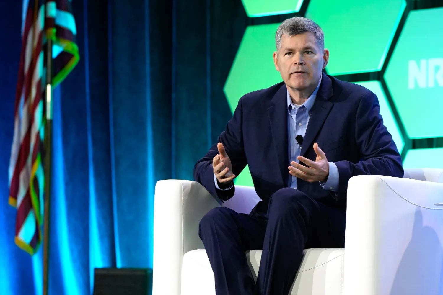 A retail asset protection expert speaks while seated on the NRF Protect stage. In the background, there is the NRF PROTECT hexagon and an American flag.