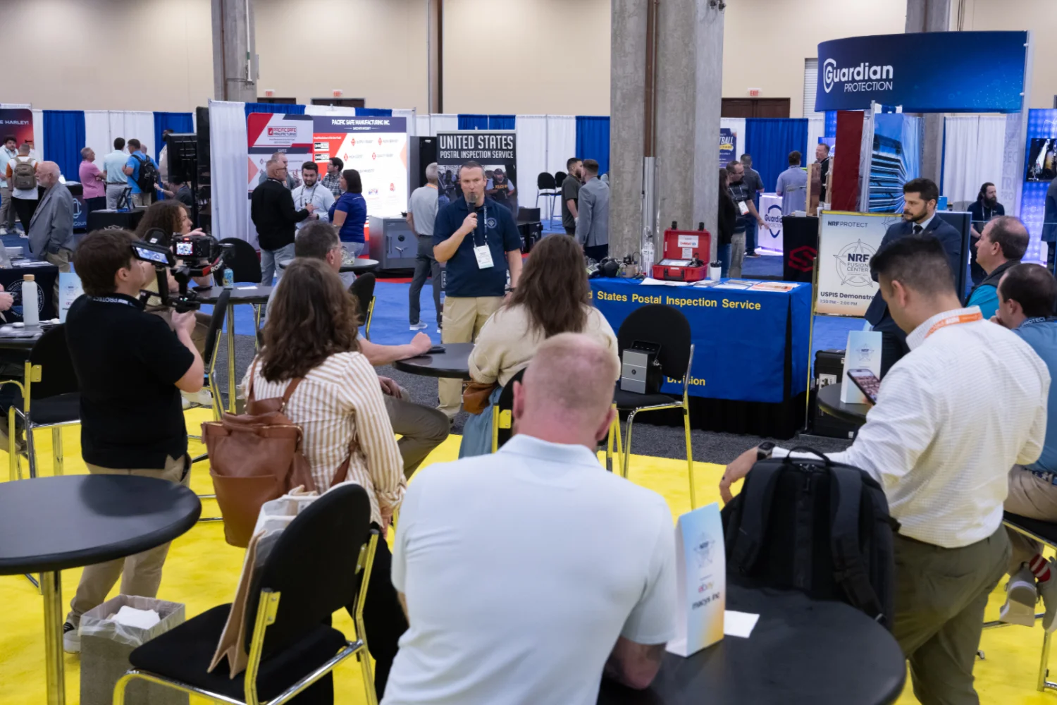 People attending NRF Protect Fusion Center are gathered around a speaker in front of a United States Postal Inspection Service booth.