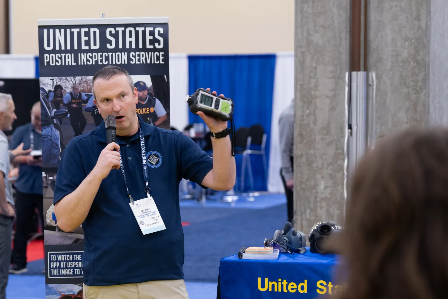 A representative from the US Postal Service Inspection Service speaks to a small crowd for a demonstration of their technology while at the NRF PROTECT EXPO floor.