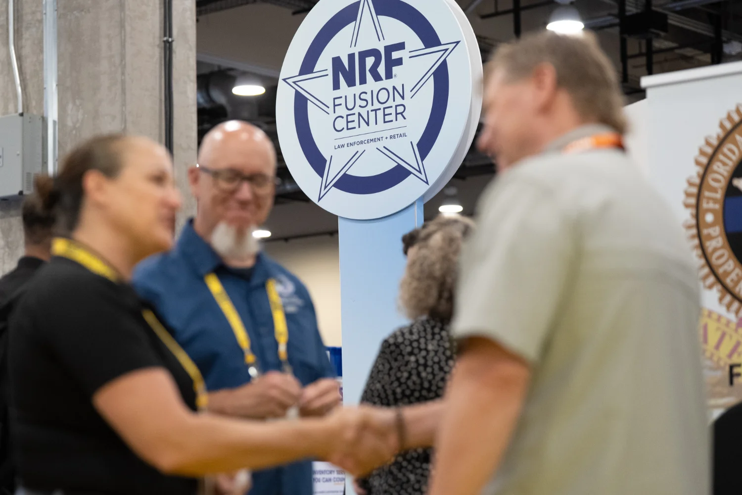 NRF Protect Fusion Center attendees shake hands underneath the Fusion Center's logo.