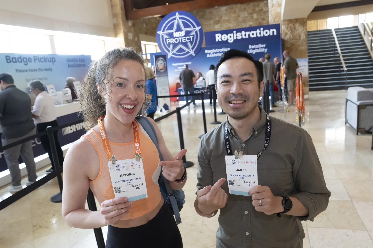 Two NRF Protect attendees proudly hold up their NRF PROTECT badges as they complete their conference registration.