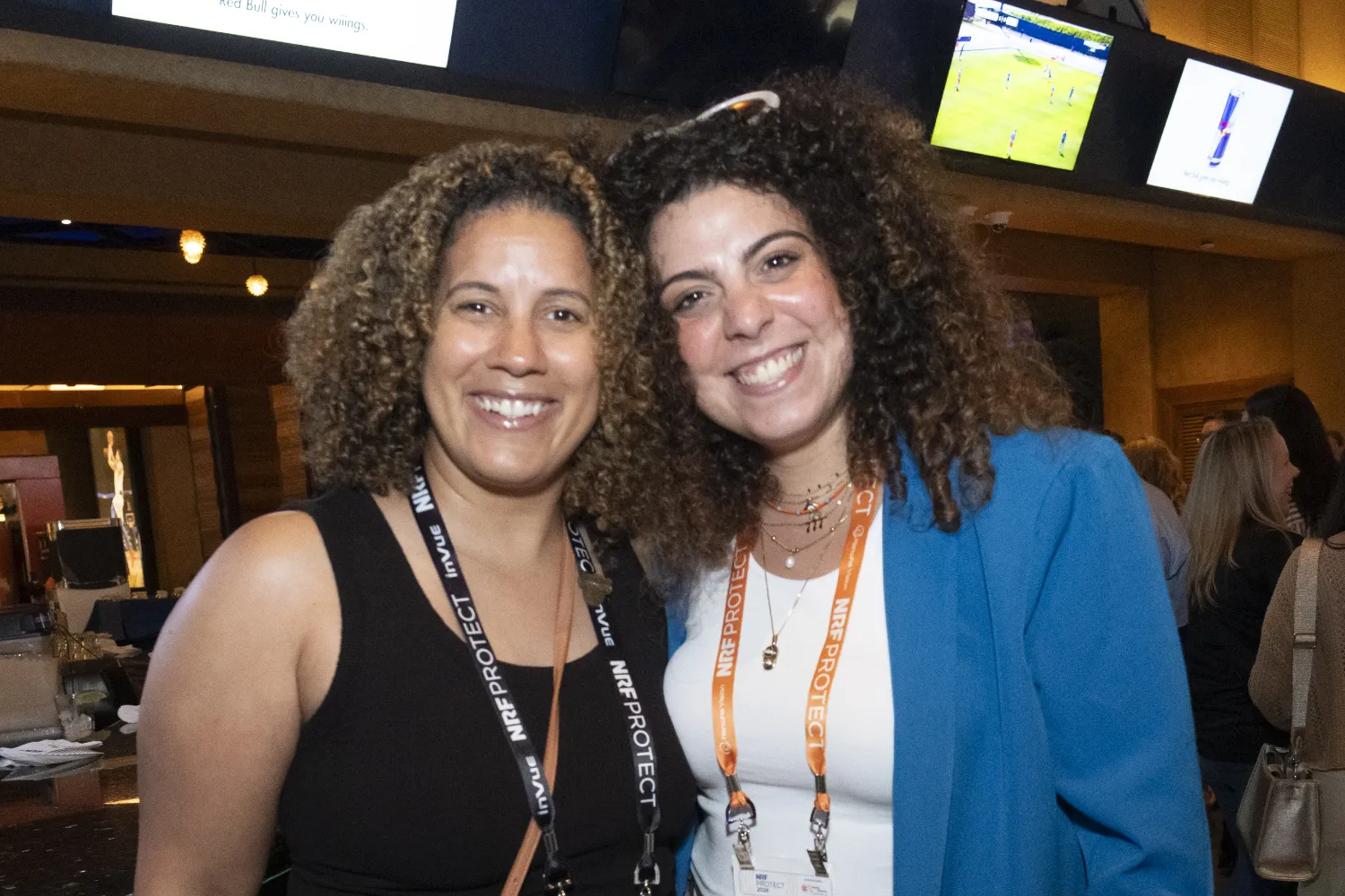 Two conference attendees wearing NRF Protect lanyards pose together at a networking event.