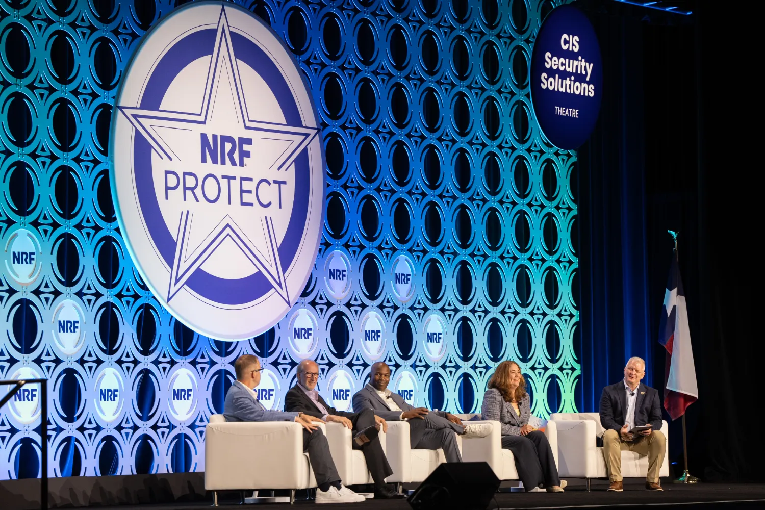 From the NRF PROTECT stage, four speakers and one moderator sit in plush, white chairs during a live discussion about the loss prevention and retail security industry.