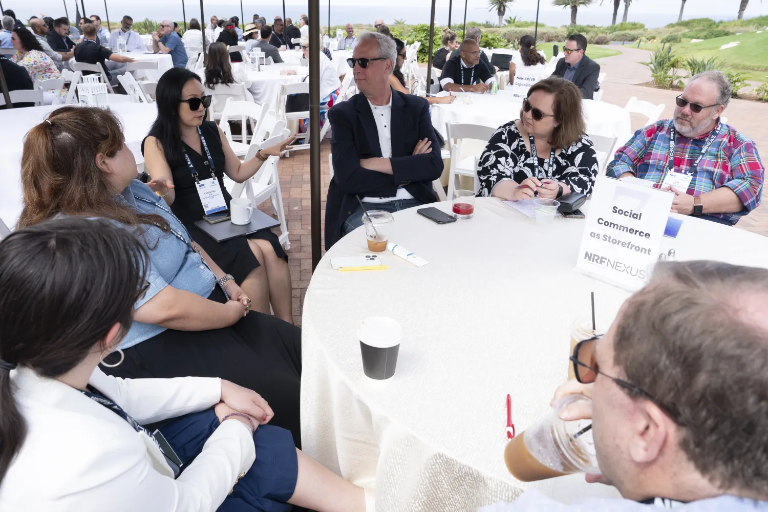 Seven retail experts attending NRF Nexus sit at a round table, listening to a colleague that is discussing the tables's assigned topic: social commerce as storefront.