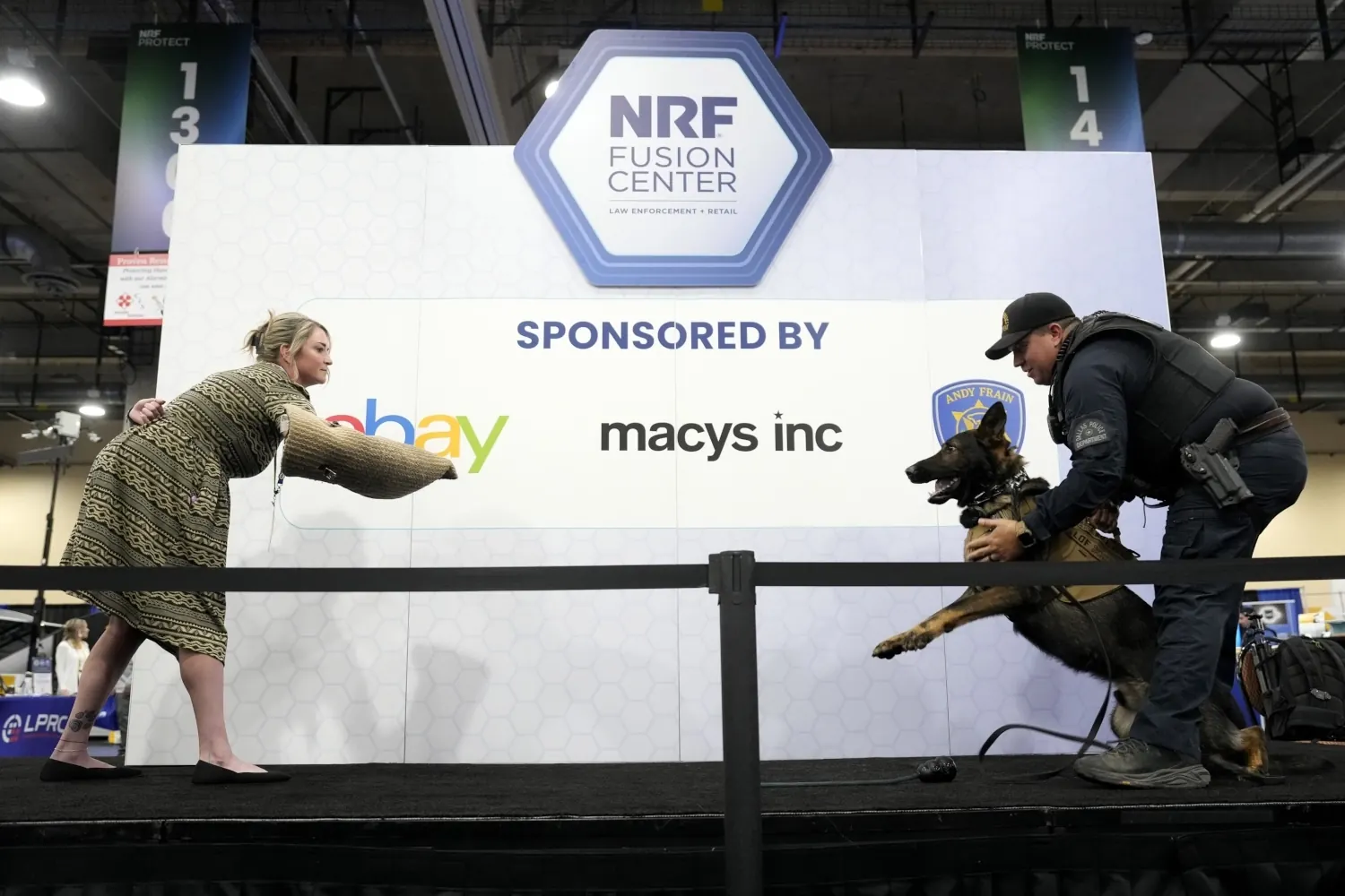 NRF PROTECT Expo floor demonstration of a police do about to perform an arm takedown of a woman. The woman is wearing protective gear on her arm. The dog is being held by a law enforcement officer in tactical gear.