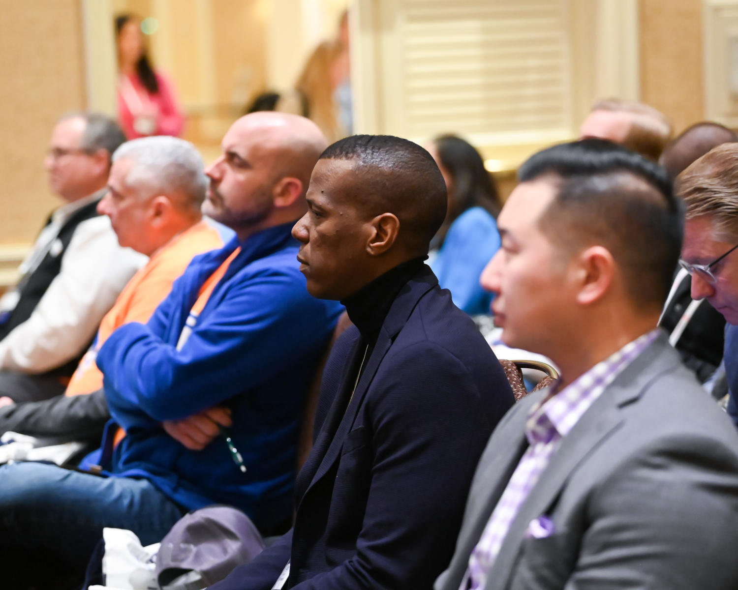 A group of attendees seated in a well-lit conference hall, attentively watching a panel discussion on stage.